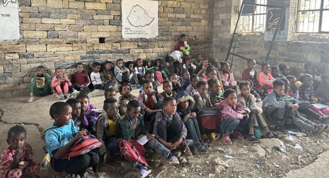 Students seated on the floor of a stone-walled classroom in Tigray